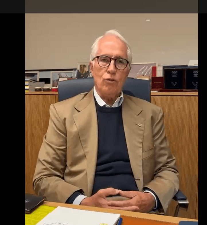 Giovanni Malagò seduto alla scrivania del suo ufficio, con le mani intrecciate, mentre parla in un videomessaggio